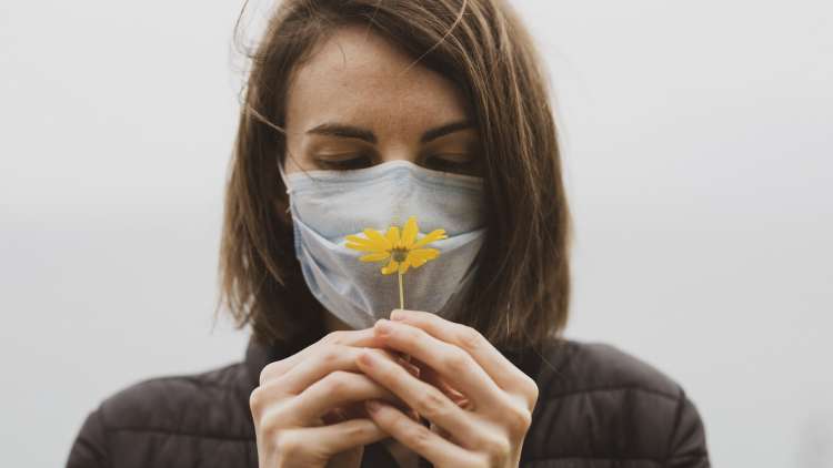 Woman smelling flower through COVID mask